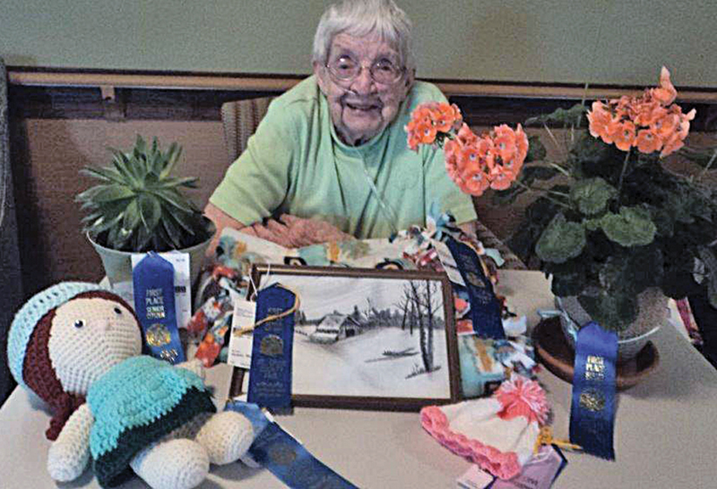 Ruth Huber poses with all her handiwork and plants, one of which is named “Ollie”, and her baby hat which won her a champion ribbon at the county fair.