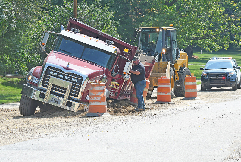 THAT SINKING FEELING — The driver of a dump truck belonging to Wirth Excavating of Ridgeland inspects his truck after it sank into the soft gravel on 1st Street in Glenwood City last Friday morning, August 20. The incident took place near St. John the Baptist Catholic Church where a water main was recently replaced following a break. Apparently, the ground was still saturated with water causing the truck that was filled with gravel to sink up to its wheel wells on the driver’s (left) side. It took a pair of heavy-duty tow trucks and a couple of hours to extricate the truck from the watery gravel. —photo by Shawn DeWitt