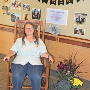 RETIREMENT GIFT — Doris Berends shown sitting in front of her retirement display, testing out the rocking chair presented to her by Glenhaven. —photo by Missy Klatt