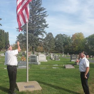 DONATION - An anonymous donation of a U.S. flag was presented to the Glenwood City Cemetary Board to fly at the Glenwood City Cemetery. Doug Hill, left, is seen raising the new flag while Marvin Booth salutes. —photo by Carlton DeWitt