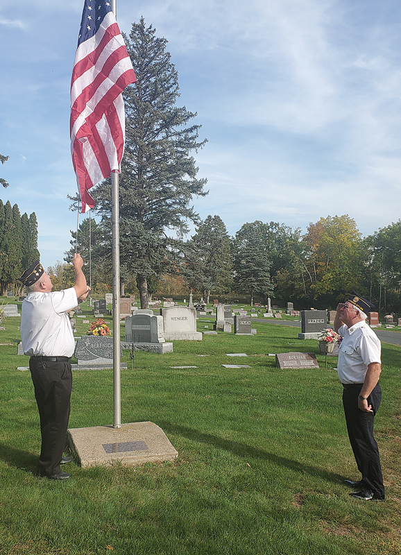 DONATION - An anonymous donation of a U.S. flag was presented to the Glenwood City Cemetary Board to fly at the Glenwood City Cemetery. Doug Hill, left, is seen raising the new flag while Marvin Booth salutes. —photo by Carlton DeWitt